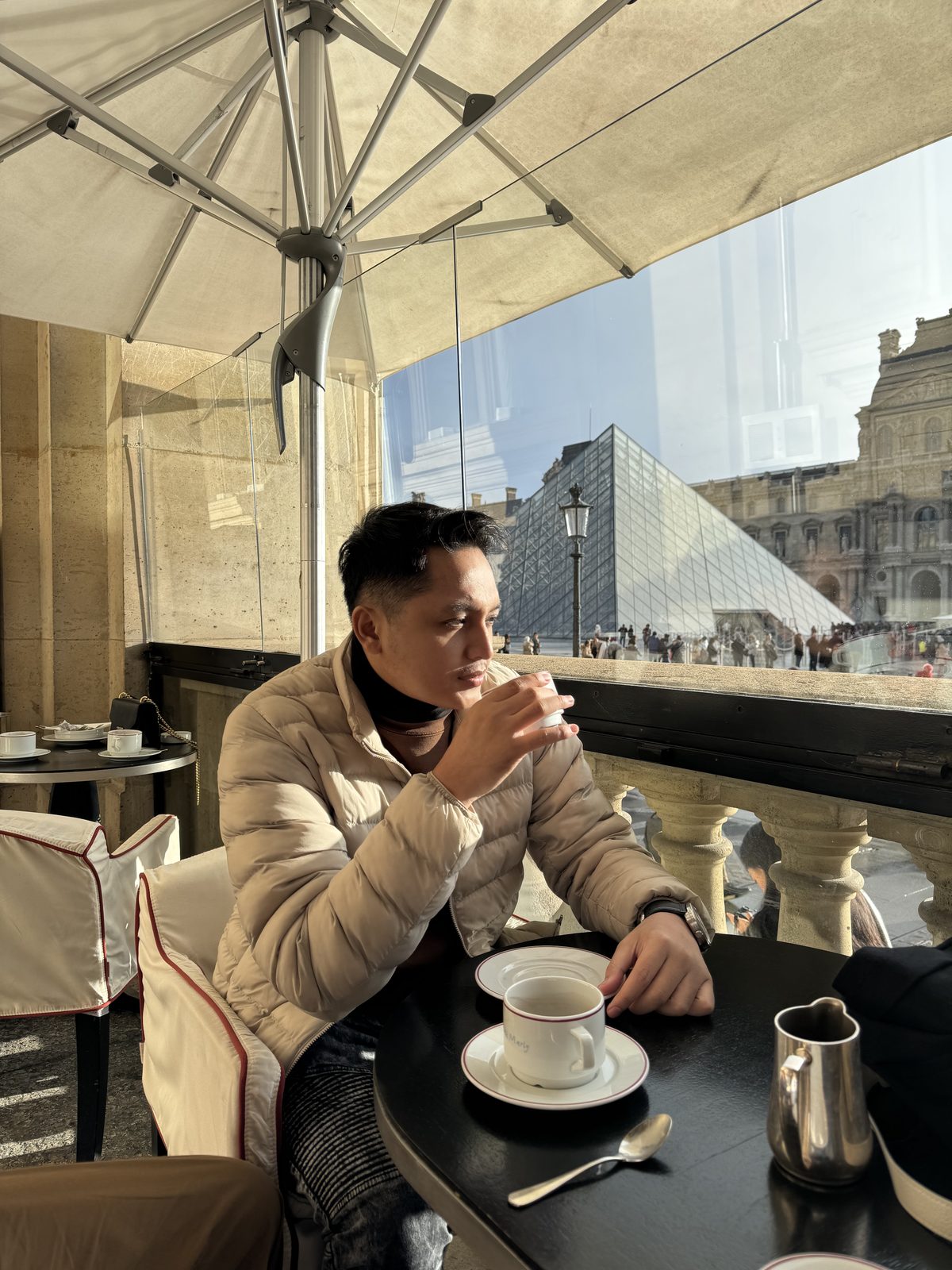 Firman menikmati kopi di teras kafe yang menghadap piramida Louvre