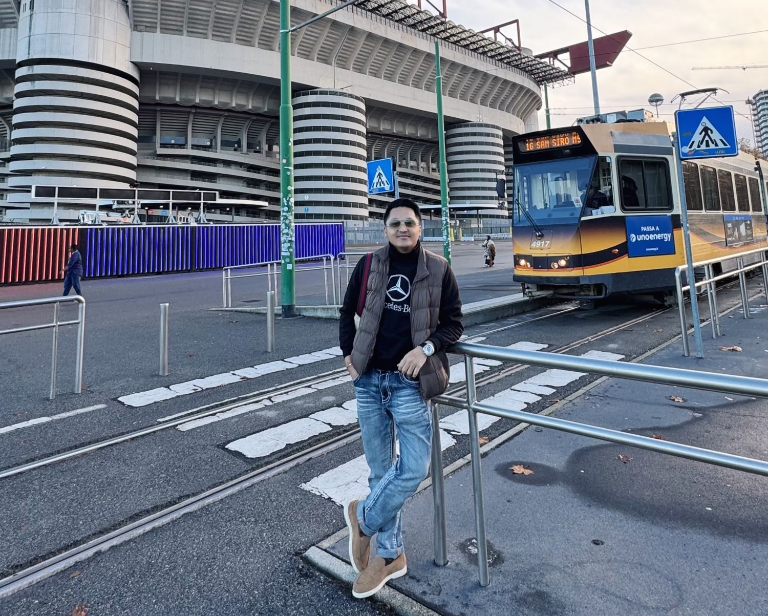 Firman bersandar di pagar di luar Stadion San Siro, Milan, dengan trem kuning di belakangnya